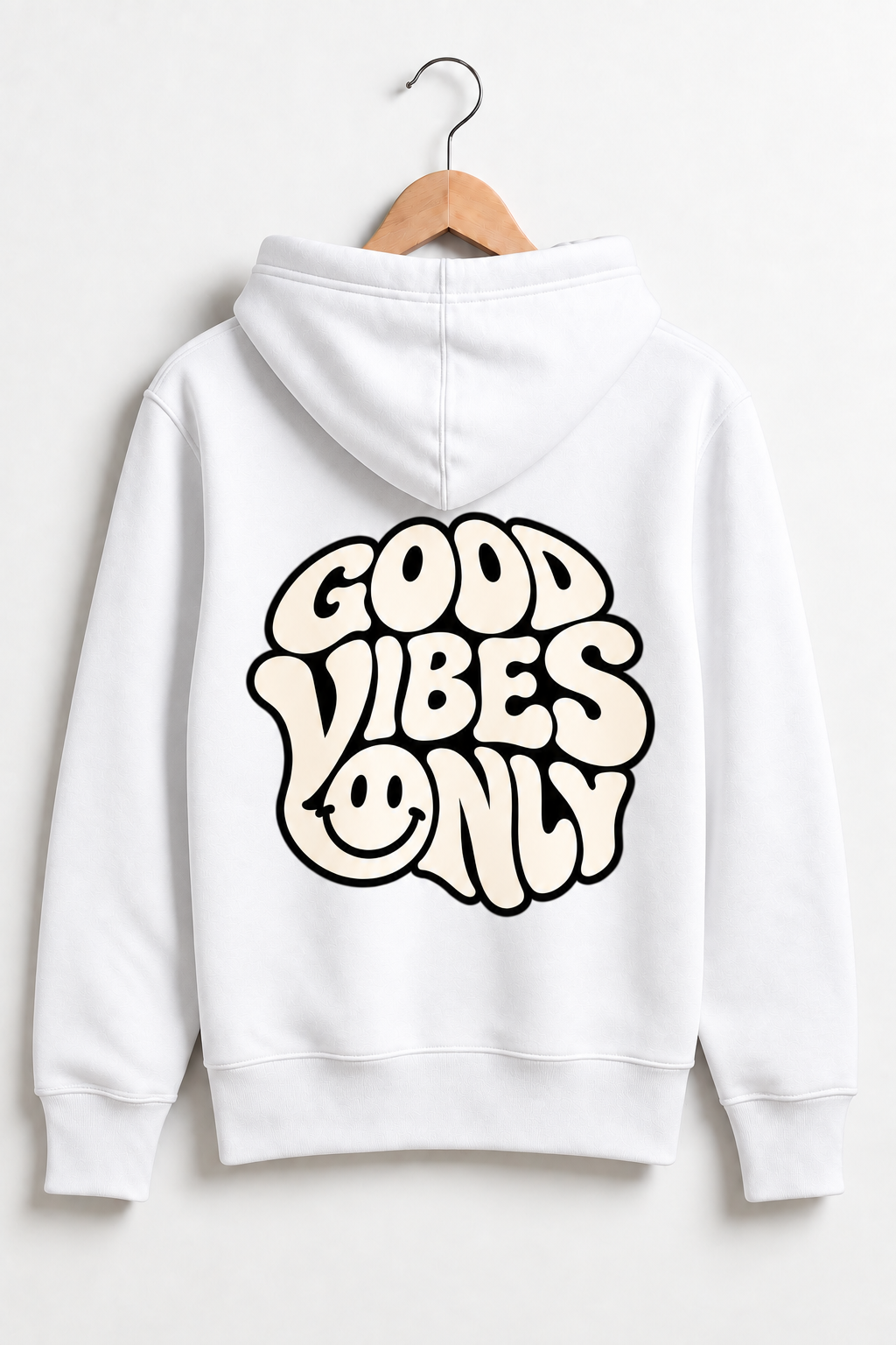 A white pullover hoodie hanging on a wooden hanger against a light gray wall, showing the back with a large retro-style graphic that reads 'GOOD VIBES ONLY' in cream lettering with black outlines and a smiley face.