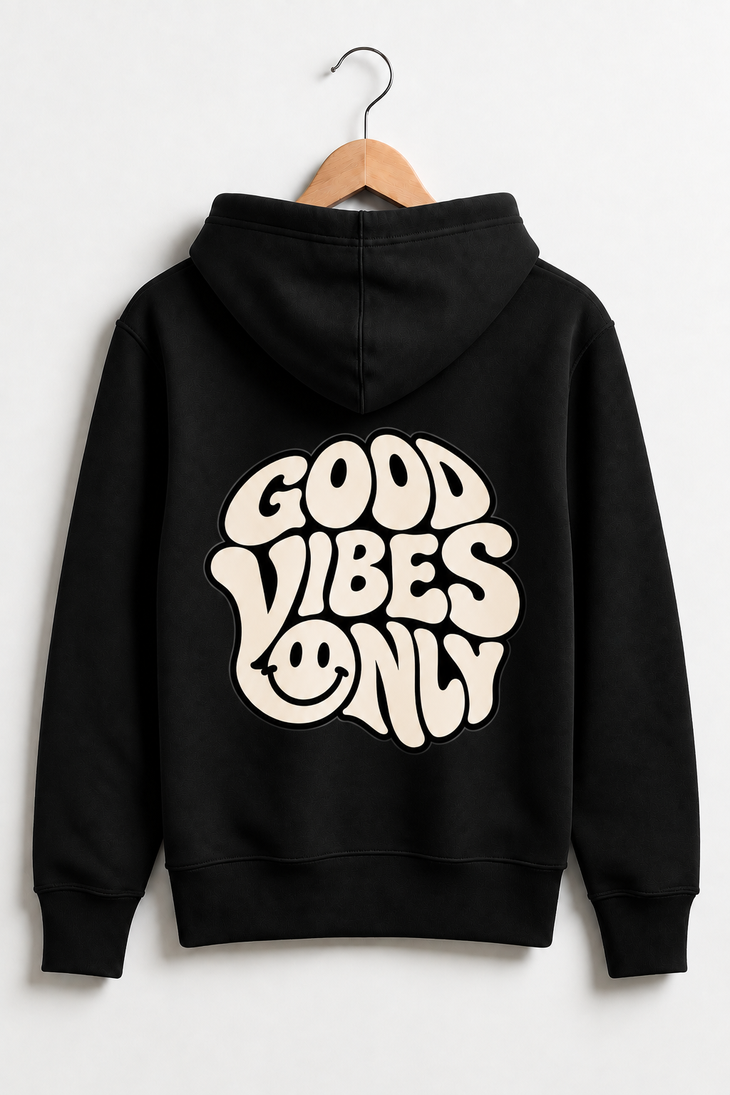 A black pullover hoodie hanging on a wooden hanger against a light gray wall, shown from the back with a large cream-colored retro graphic that reads 'GOOD VIBES ONLY' and a smiley face.
