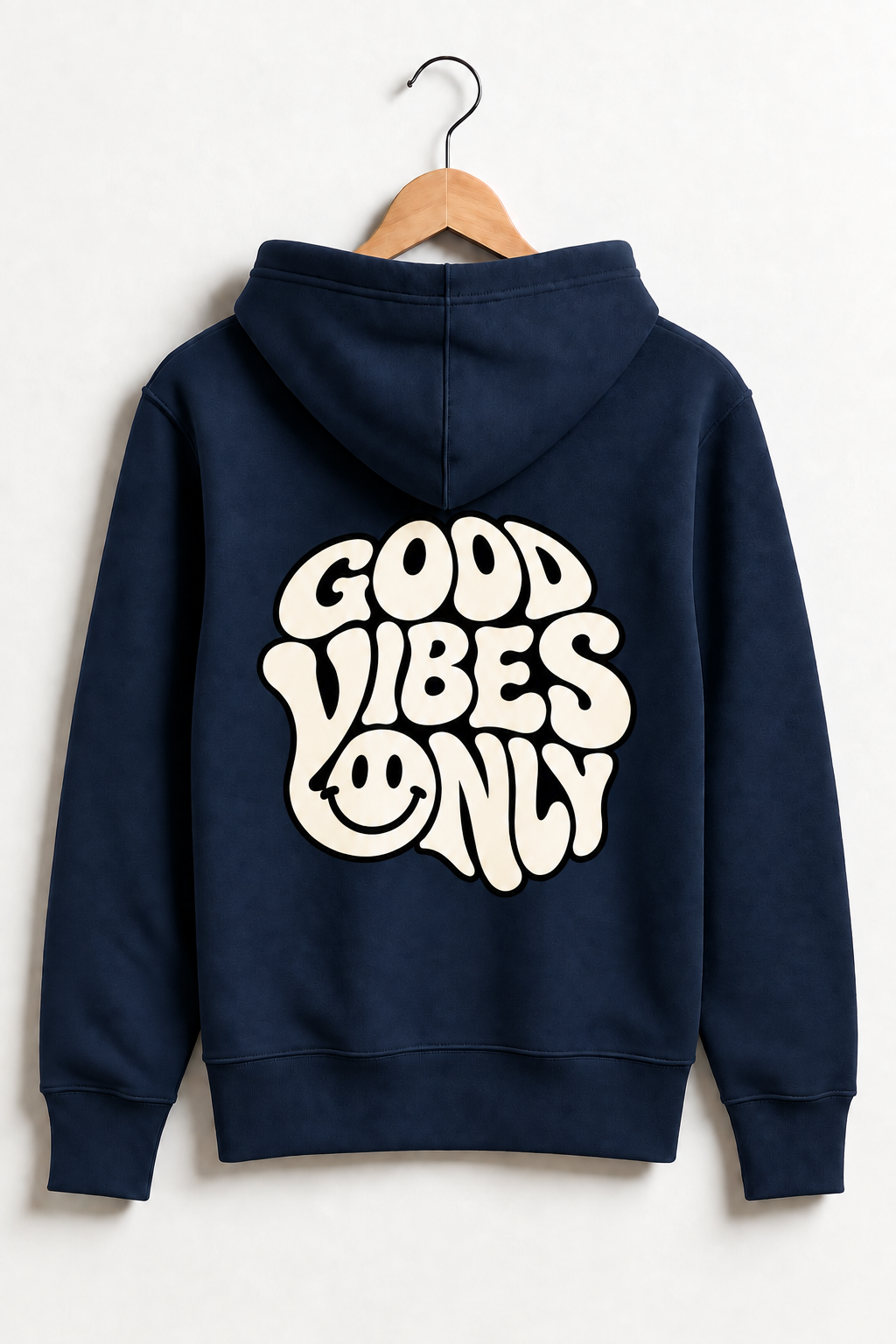 A navy blue hoodie hanging on a wooden hanger against a light gray wall, featuring a large retro-style cream graphic on the back that reads 'GOOD VIBES ONLY' with a smiley face.