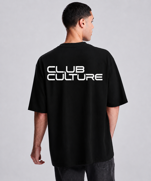 A man viewed from the back wearing a black oversized t-shirt with 'CLUB CULTURE' printed in bold white letters across the upper back, paired with dark gray jeans against a light gray studio background.