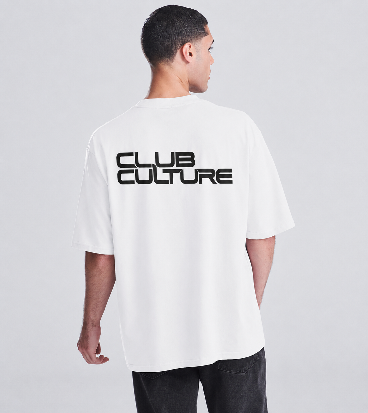 A man wearing a white short-sleeve t-shirt with a bold black 'CLUB CULTURE' graphic printed across the back, shown from a rear three-quarter view against a light gray studio background.