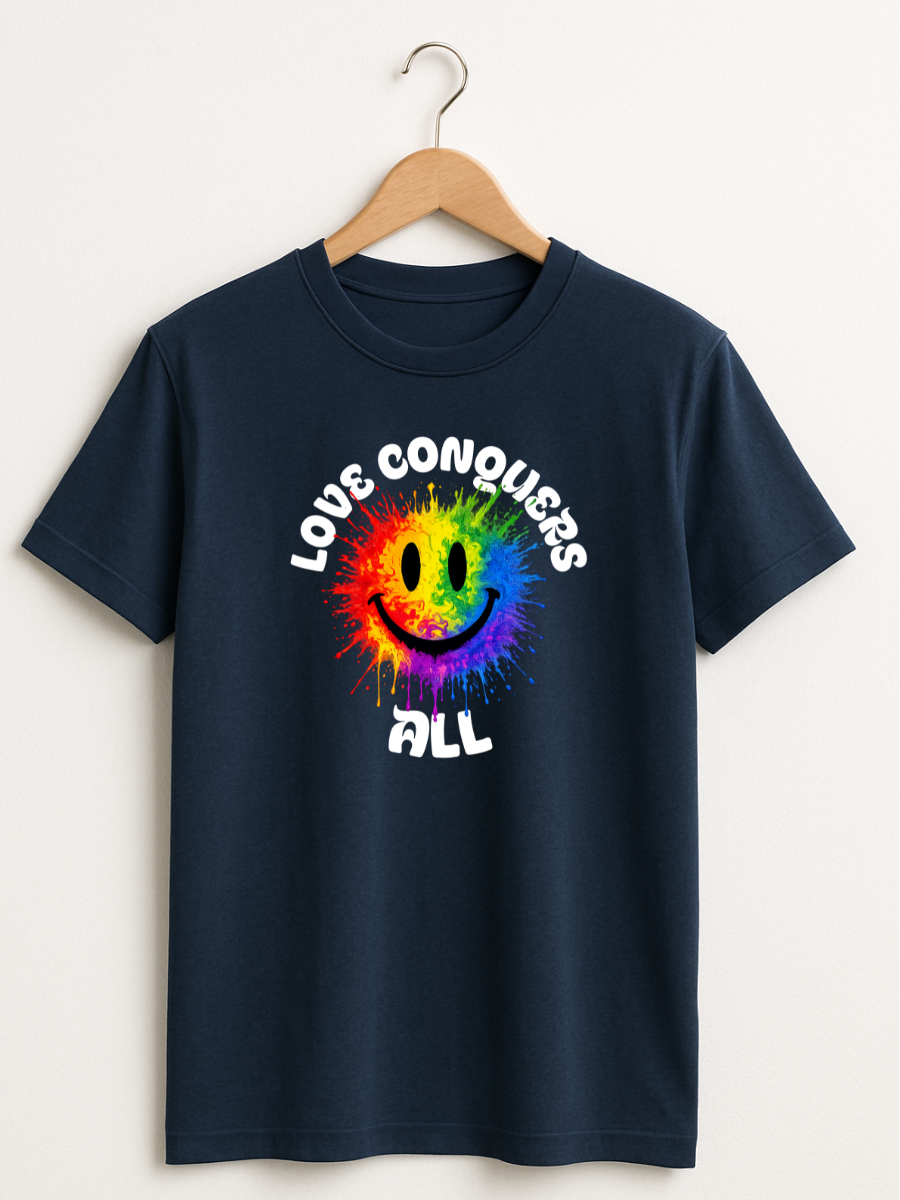 A navy blue short-sleeve t-shirt hanging on a wooden hanger against a light beige wall. The shirt features a colorful graphic of a rainbow smiley face with the words 'LOVE CONQUERS ALL' printed in white around it.