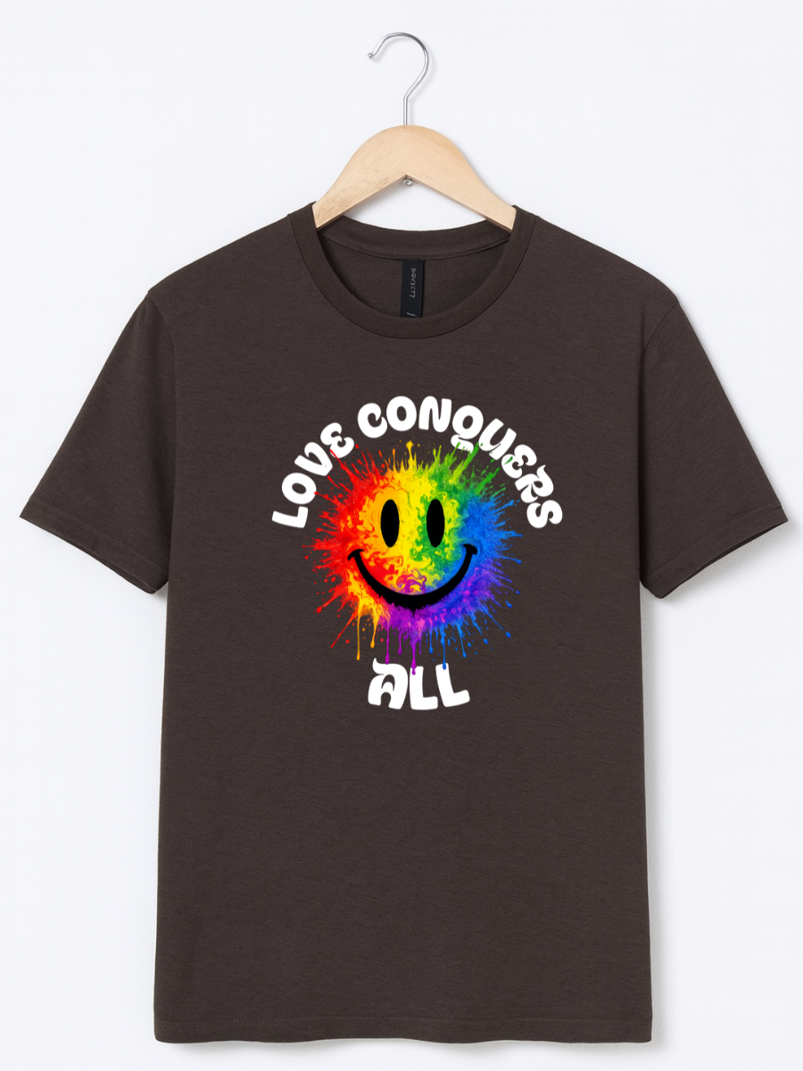 A dark brown short-sleeve t-shirt hanging on a wooden hanger against a light gray background. The shirt features a colorful rainbow tie-dye smiley face graphic with the white text 'LOVE CONQUERS ALL' arched above and below the face.