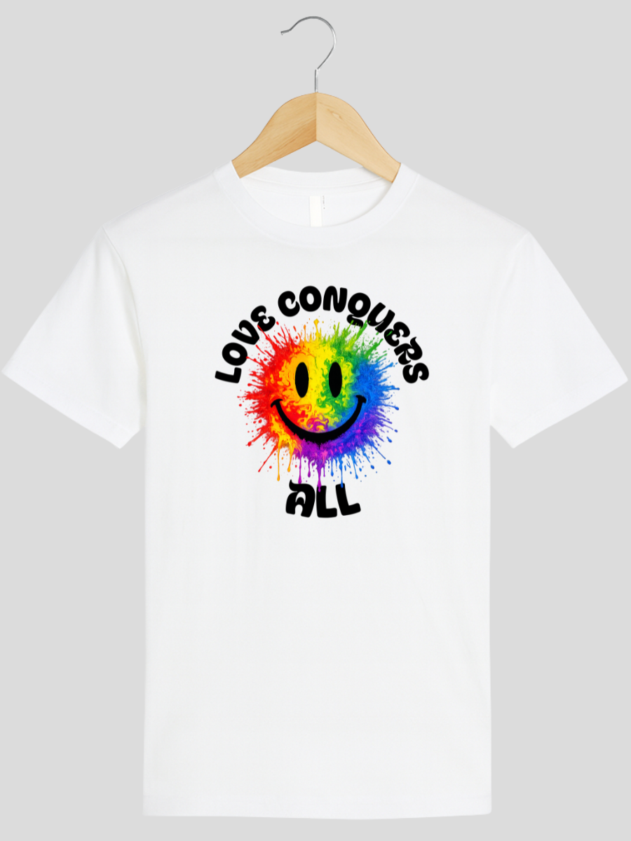 A white short-sleeve crewneck t-shirt hanging on a wooden hanger against a light gray background. The shirt features a colorful graphic in the center with a rainbow-colored smiley face and the words 'LOVE CONQUERS ALL' in black.