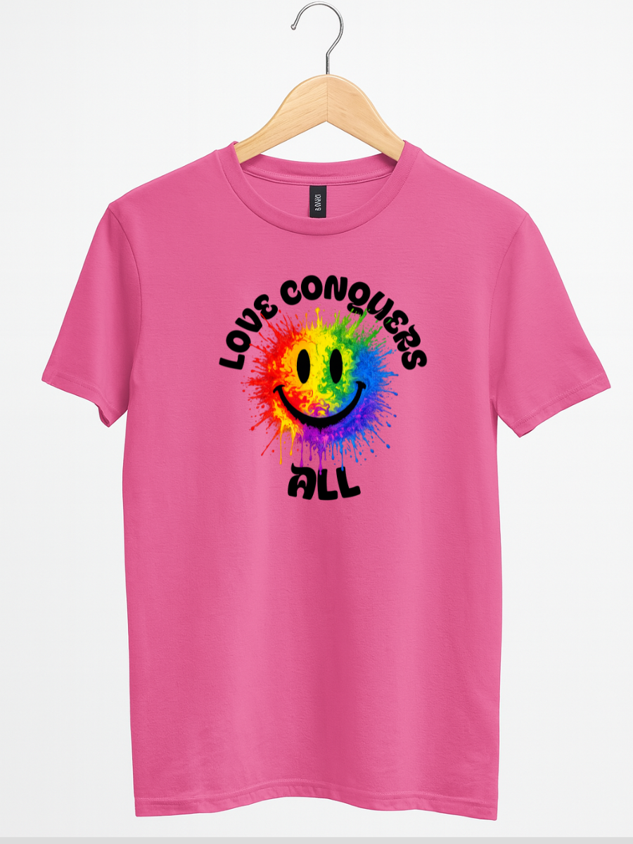 A pink short-sleeve t-shirt hanging on a wooden hanger against a white background. The shirt features a colorful rainbow smiley face graphic with the words 'LOVE CONQUERS ALL' printed in black around it.