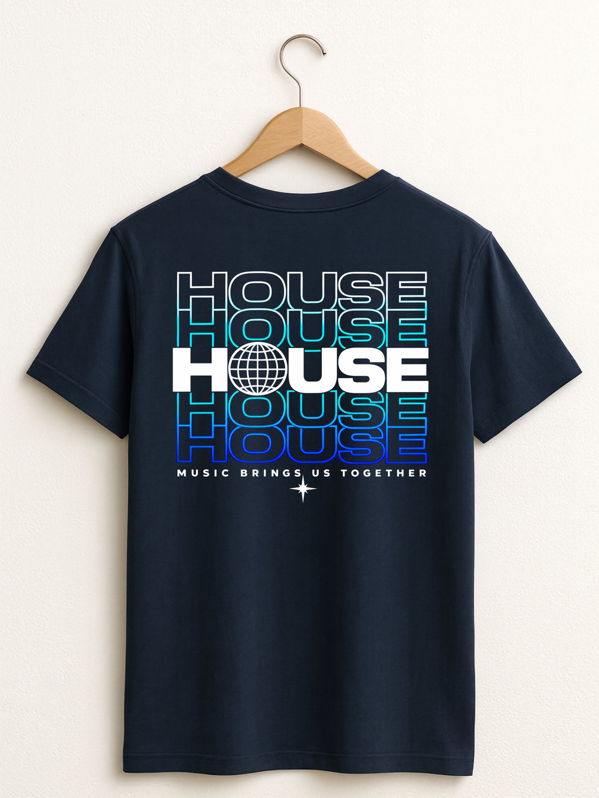 A navy blue short-sleeve t-shirt hanging on a wooden hanger against a light beige wall. The back of the shirt features a large graphic print with the word 'HOUSE' repeated in stacked, fading text (from cyan to blue to purple) in white and blue outlines, with 'MUSIC BRINGS US TOGETHER' printed below.
