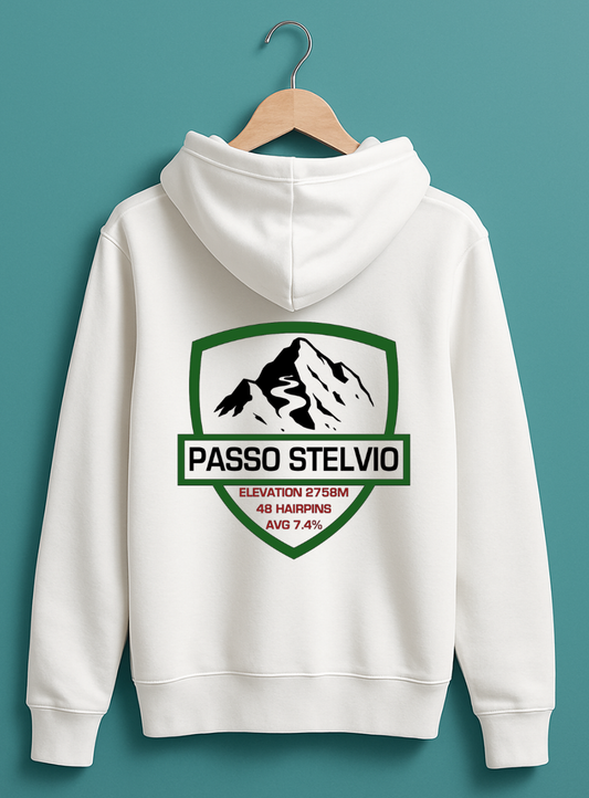 White hoodie displayed on a wooden hanger against a teal background, featuring a bold Passo Stelvio mountain crest graphic on the back with elevation, hairpins, and average gradient details.