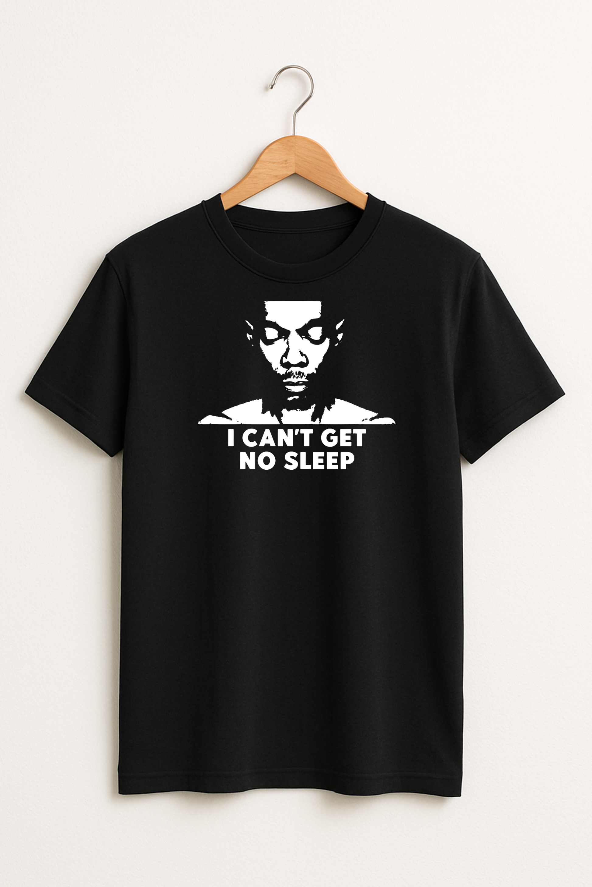 Black T-shirt hanging on a wooden hanger with a white graphic of a face and the text “I Can’t Get No Sleep” on the front.