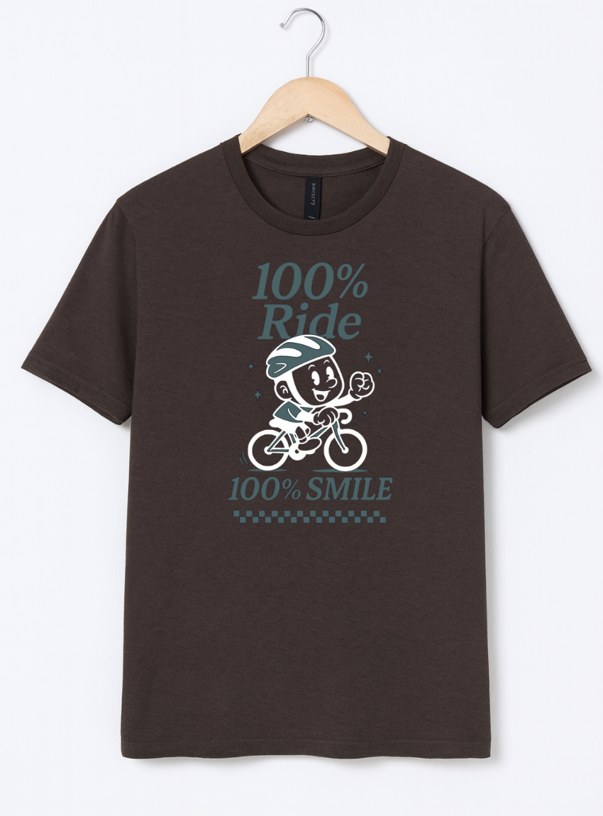 Brown t-shirt with a graphic design of a cartoon character on a bike and text '100% Ride, 100% Smile' hanging on a wooden hanger.